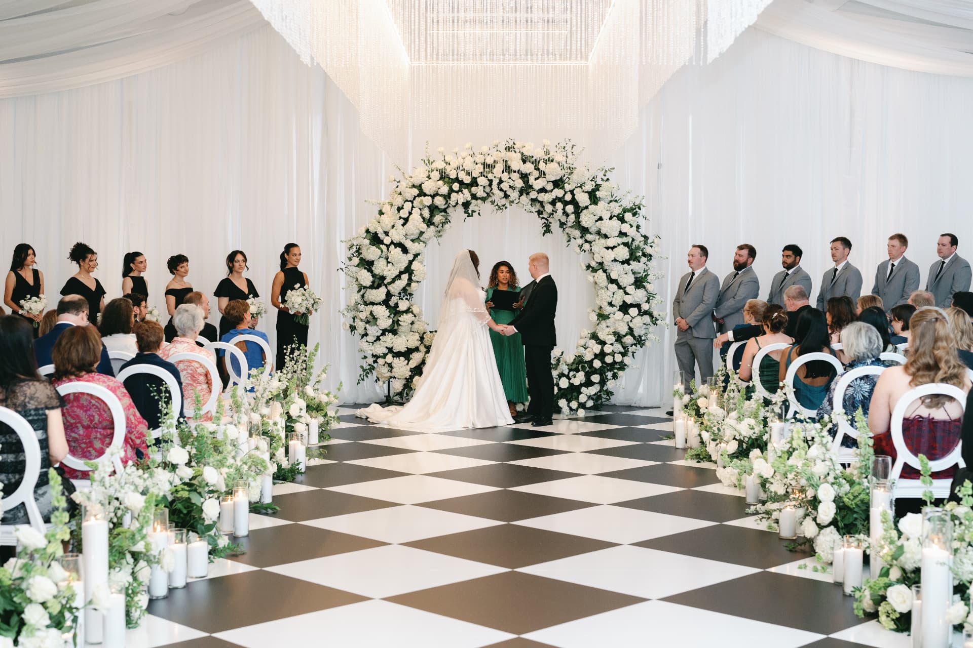 Elegant indoor wedding ceremony beneath a lush white floral arch