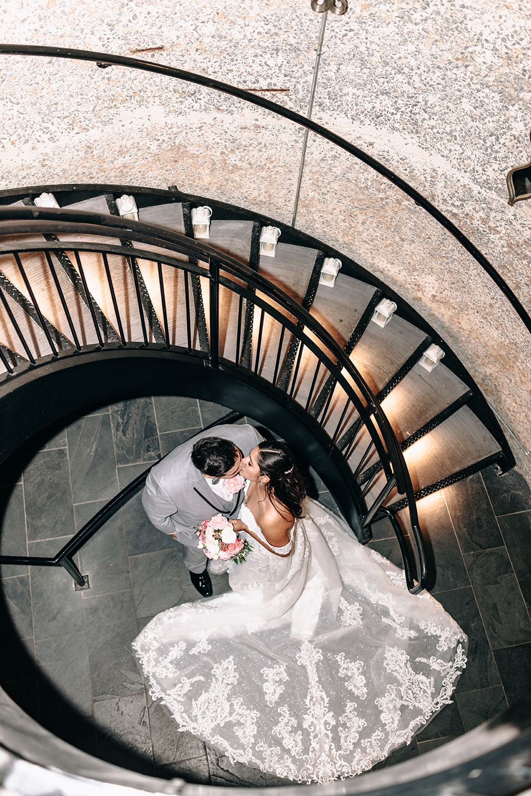 Bride and groom sharing a kiss beneath a spiral staircase